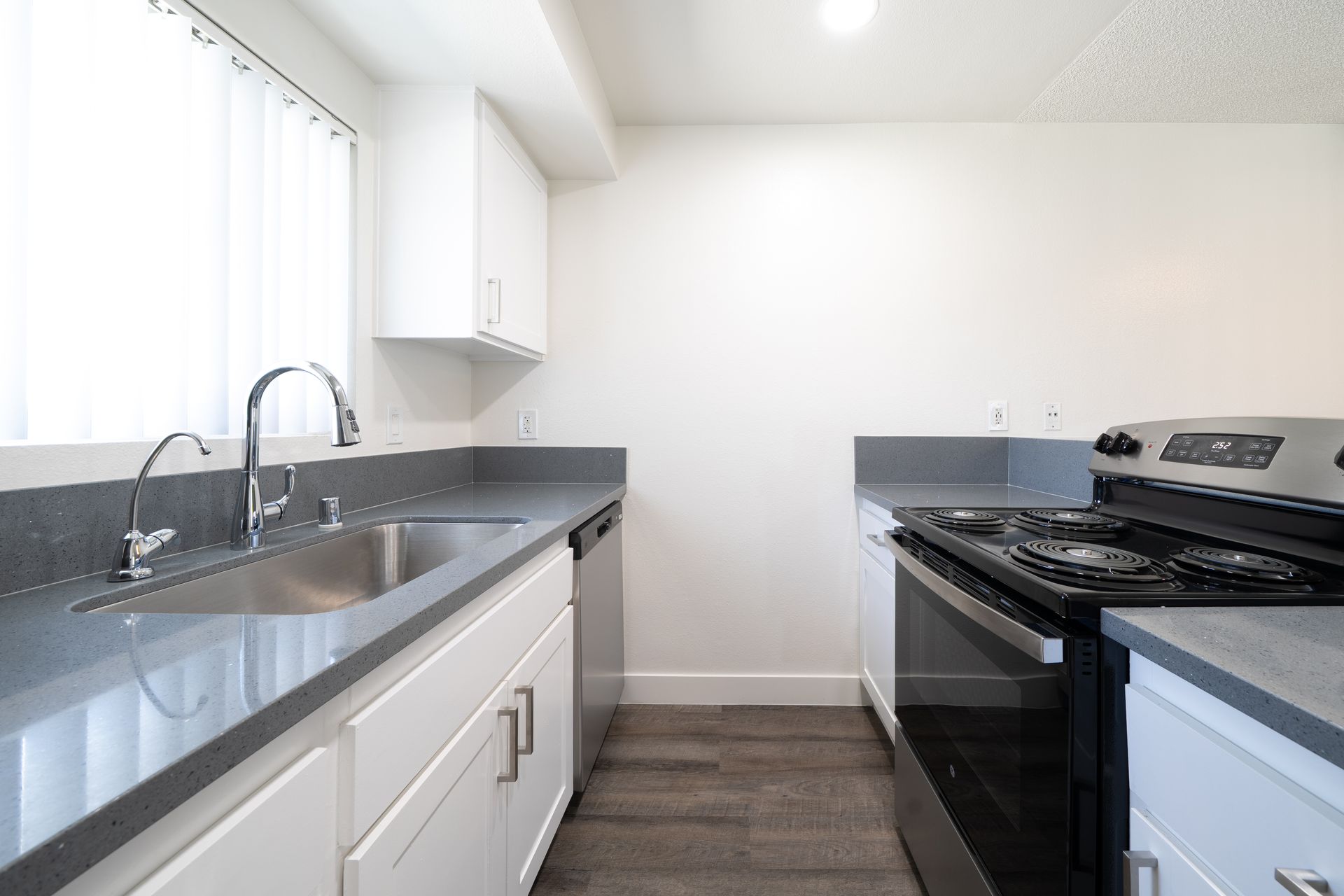 Bright white galley kitchen with gray countertops, stainless sink, and gas stove.