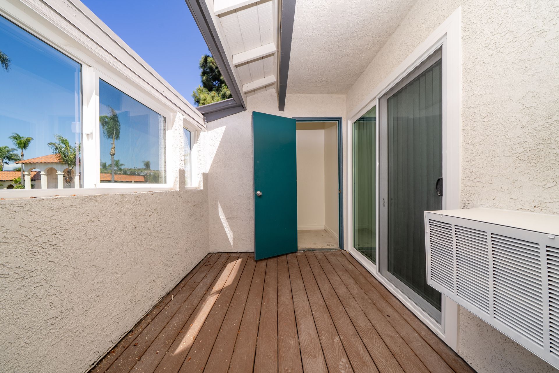 Small outdoor patio with wood decking, white walls, teal door, and sliding glass doors.