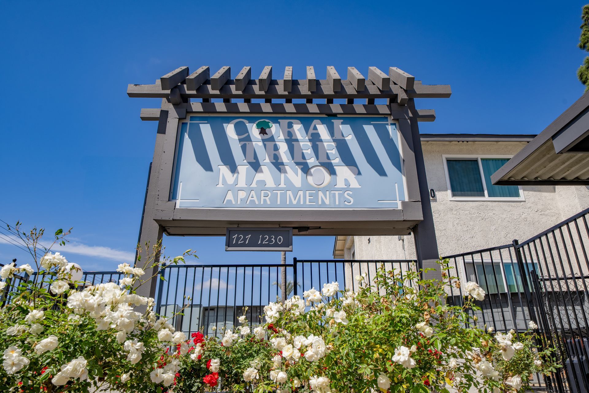 Sign for Manor Apartment Homes above white flowers under a bright blue sky