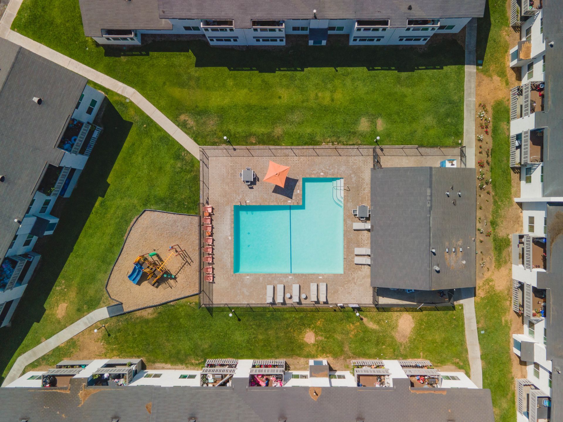 Aerial view of an apartment courtyard with a turquoise swimming pool, deck chairs, and surrounding buildings.