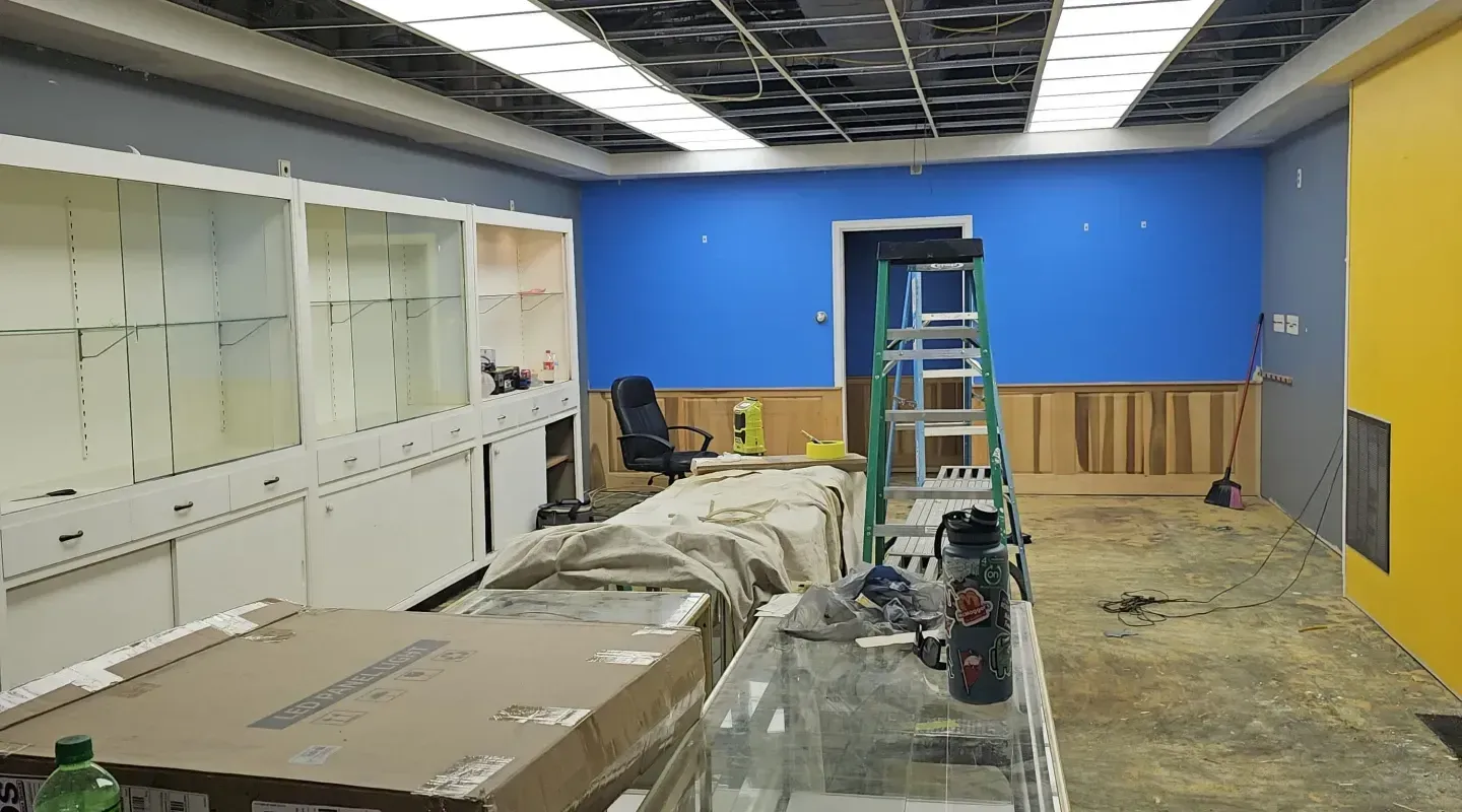 A room under renovation featuring blue walls, wood paneling, a ladder, white cabinetry, and a yellow accent wall.