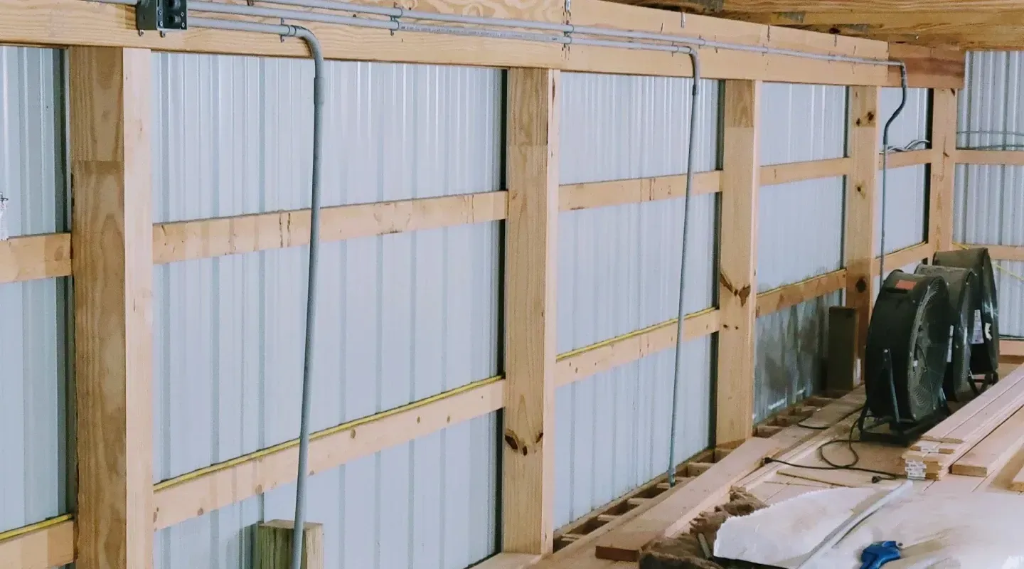 Interior view of a pole barn showing wood wall framing, metal siding, and electrical cables running along the beams.