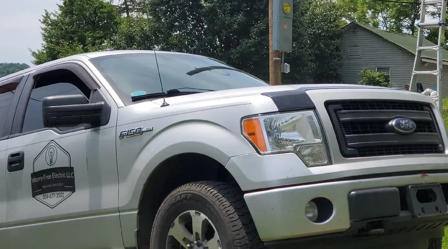 A silver Ford F-150 pickup truck with a business logo on the door, parked outdoors near a ladder.