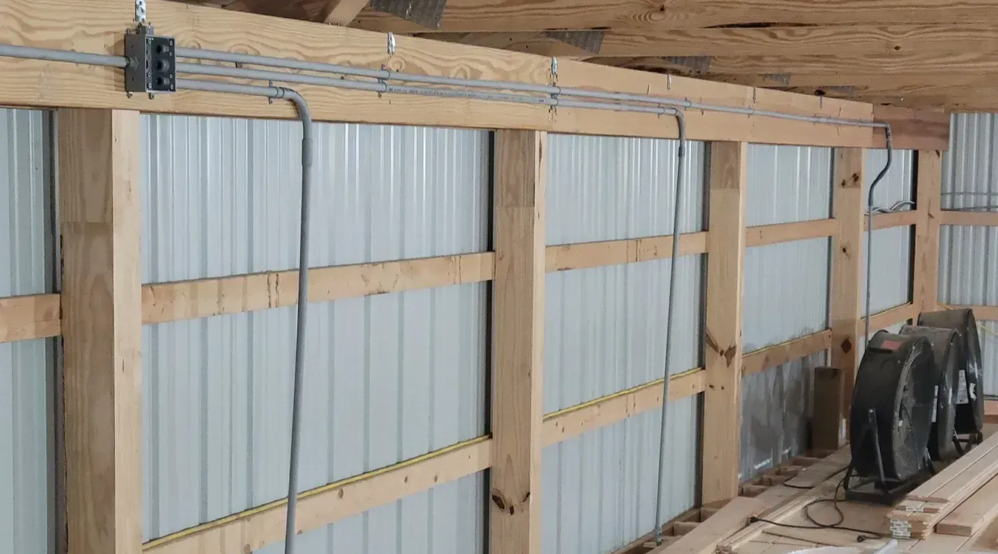 Electrical cables run along a wooden beam inside a pole barn, with a junction box and fans visible.
