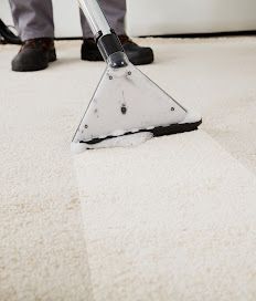 Carpet cleaning tool scrubbing a white rug near a person’s shoes