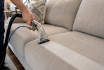 Hand using a vacuum cleaner to clean a beige sofa cushion