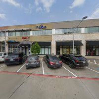 Strip mall storefronts with parked cars in front of a beige commercial building