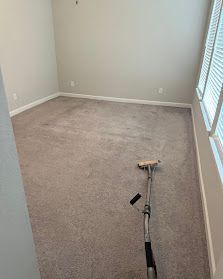 Empty beige carpeted room with a cleaning vacuum and wand on the floor near the window.