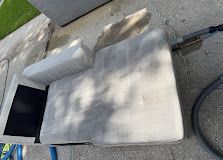 White striped patio cushion lying on a stone surface beside a black rectangular object and hose