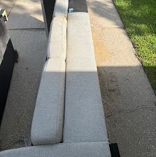 White foam barrier running along a sidewalk beside grass and parked cars in sunlight