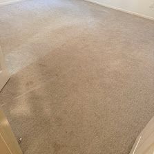 Empty beige carpeted room with white walls and baseboards, viewed from a doorway