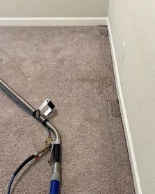 Carpeted room corner with a vacuum hose and cleaning tool on the floor near white walls.
