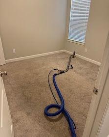 Vacuum hose on beige carpet in an empty room with closed blinds