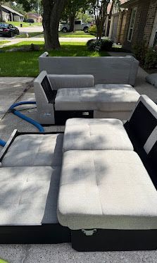 Gray and black outdoor sectional sofa on a patio, with a grassy yard and house in the background.