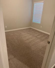 Empty beige carpeted bedroom with white walls and a window with blinds