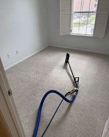 Carpeted empty room with a blue vacuum hose and cleaning tool near the window