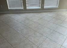 Empty beige tiled floor beside windows with closed blinds and white baseboard.