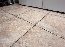 Close-up of beige tiled floor with dark grout lines and cabinet base at the top edge