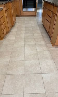 A tiled kitchen floor between wooden cabinets, leading to a doorway.