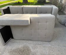 Gray L-shaped sectional sofa with built-in black side compartments on a light stone patio