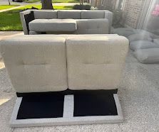 Light gray outdoor sofa with black seat cushions on a patio near grass and a house wall