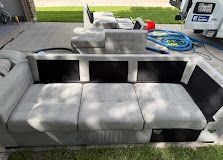 Gray sectional outdoor sofa on a patio, with black side panels and a hose in the background.