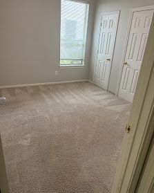Empty beige carpeted bedroom with two white closet doors and a window letting in daylight