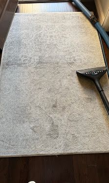 Light beige rug on a dark wood floor with a black vacuum cleaner attachment at the edge