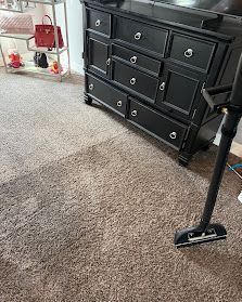 Carpeted room with a black dresser, vacuum head, and red decor on a side table.