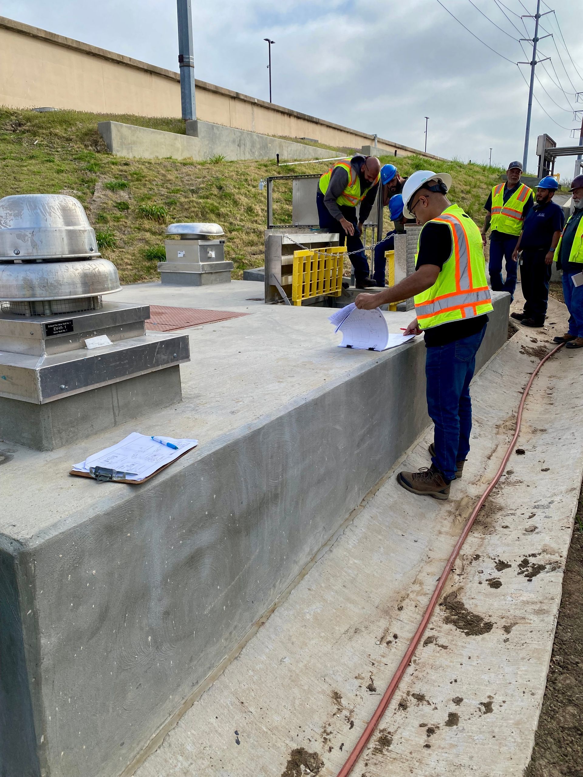 Workers in safety vests inspect rooftop equipment beside a concrete walkway.