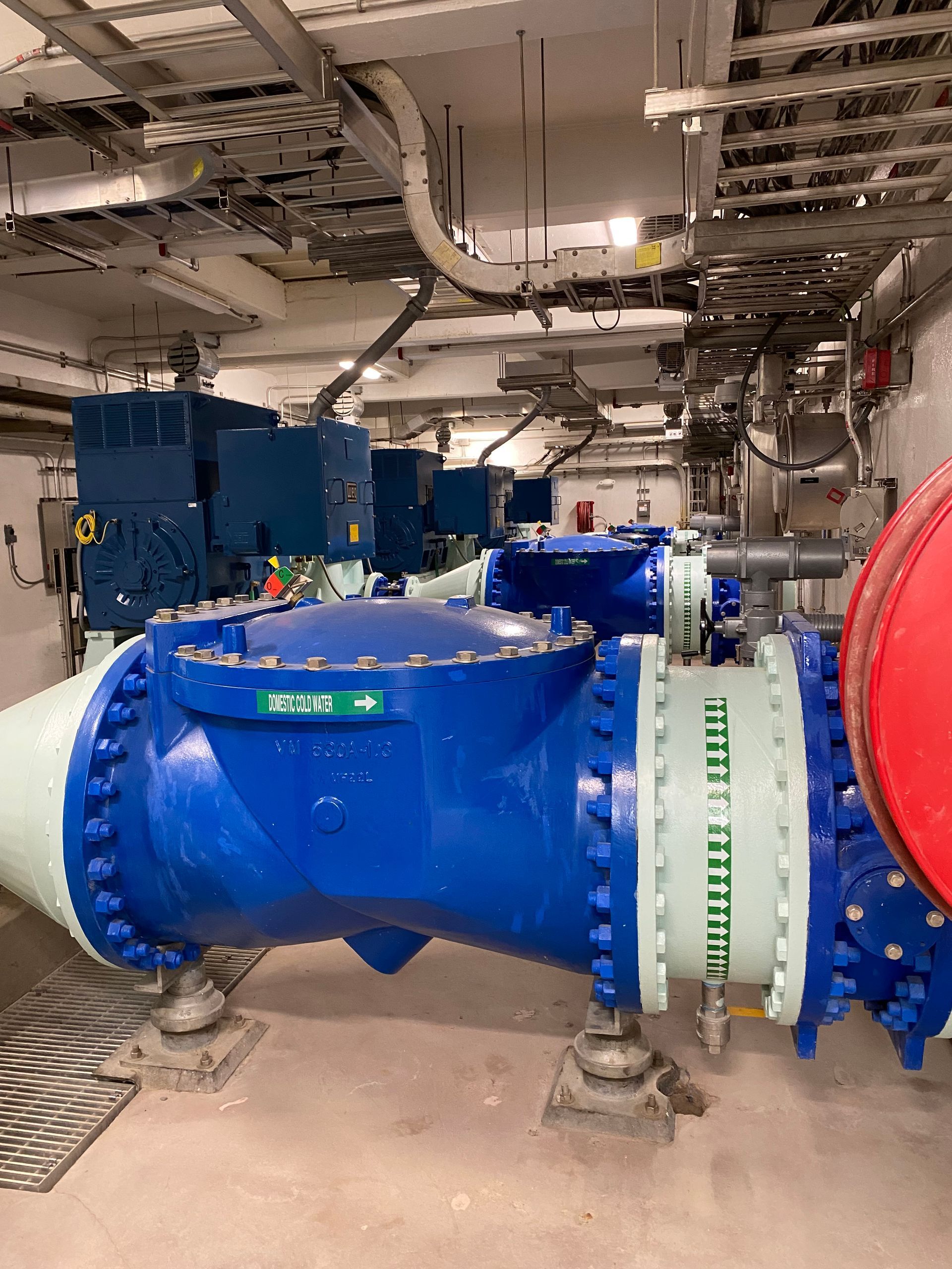 Blue industrial pipeline with large valves and machinery in a mechanical room