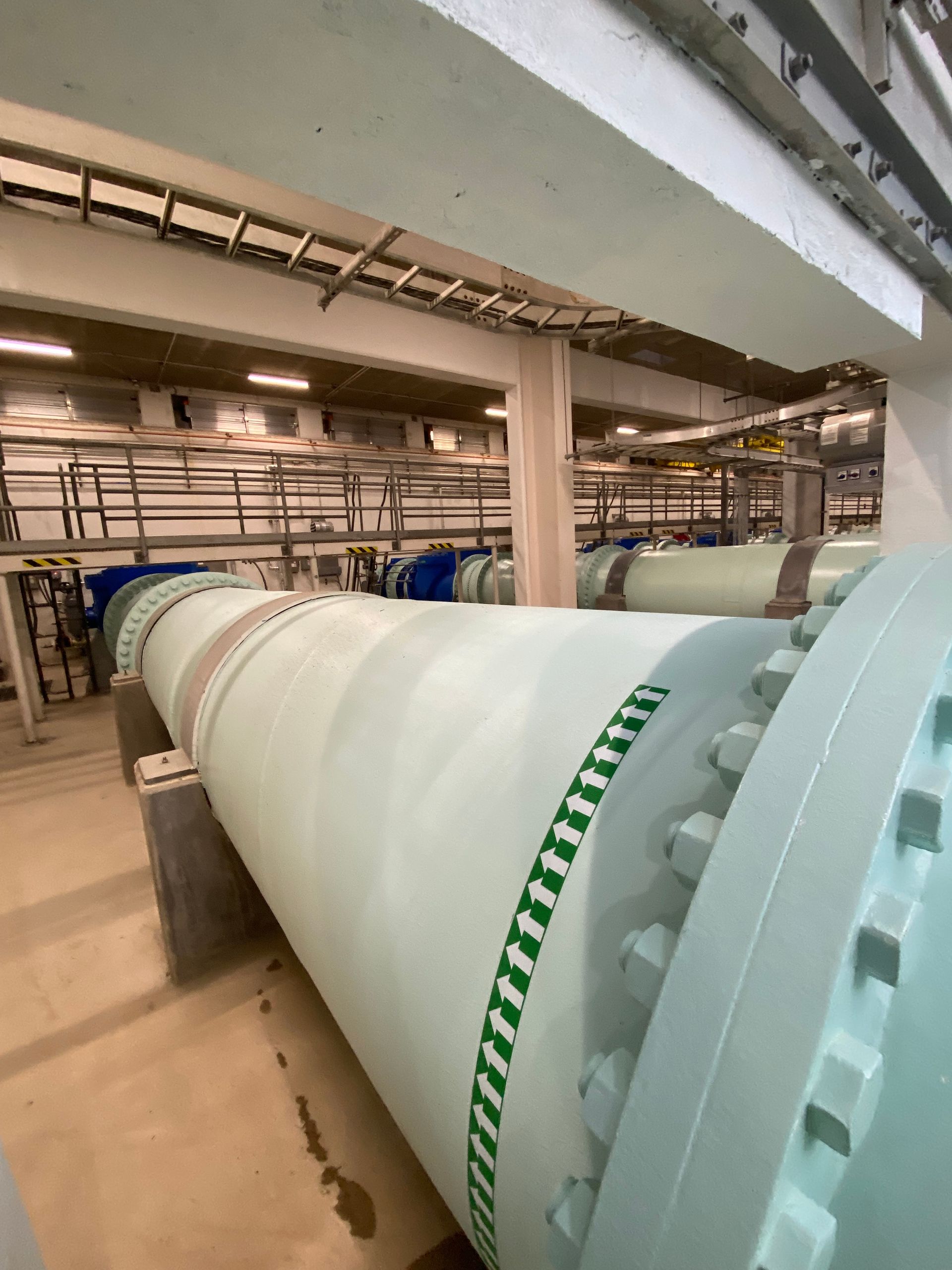 Large white industrial pipe in a plant room with exposed ceiling piping and equipment
