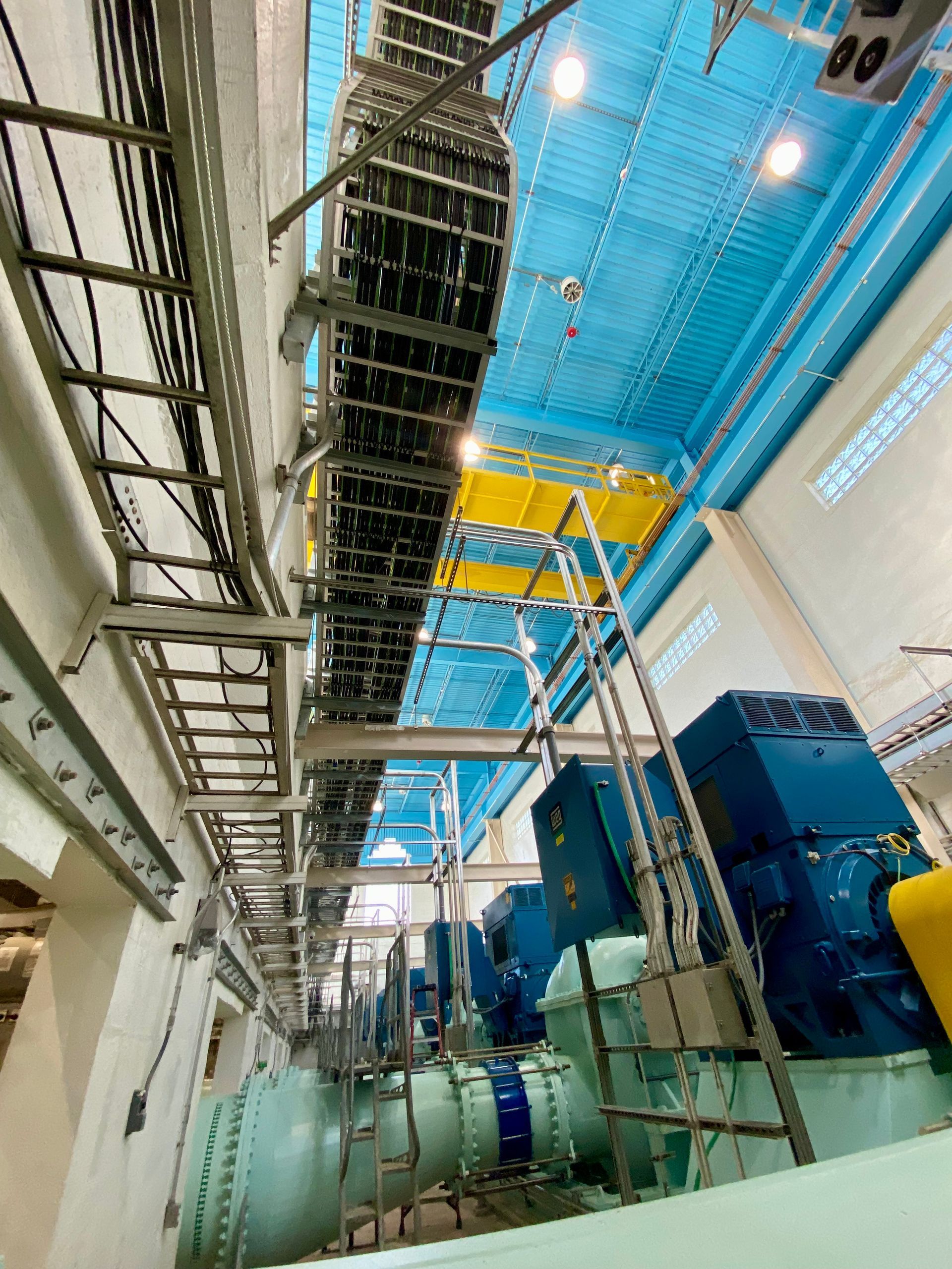 Industrial interior with blue safety netting and overhead scaffolding above large machinery and pipes