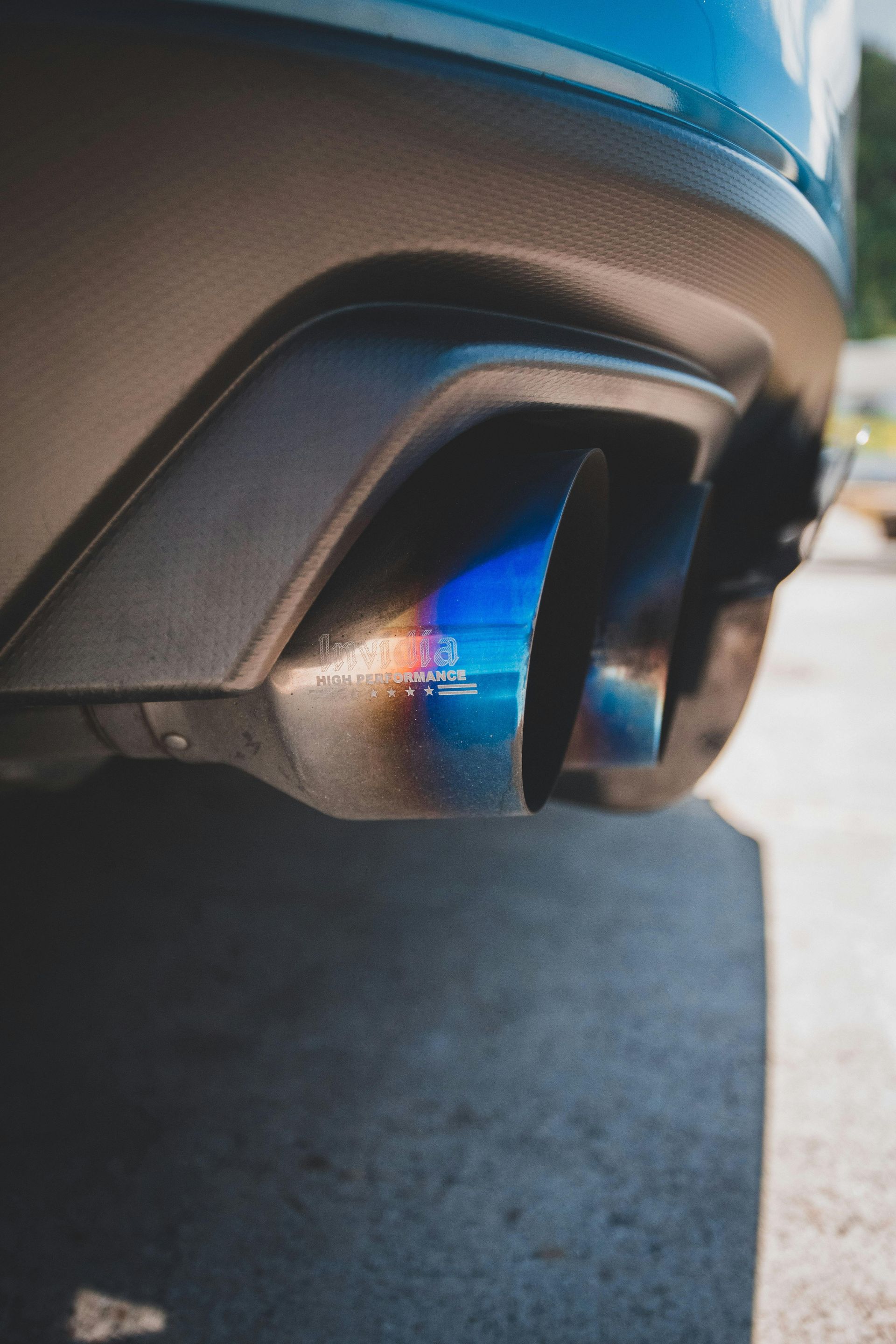 Close-up of a car’s blue-tinted exhaust tip and rear bumper, parked on pavement.