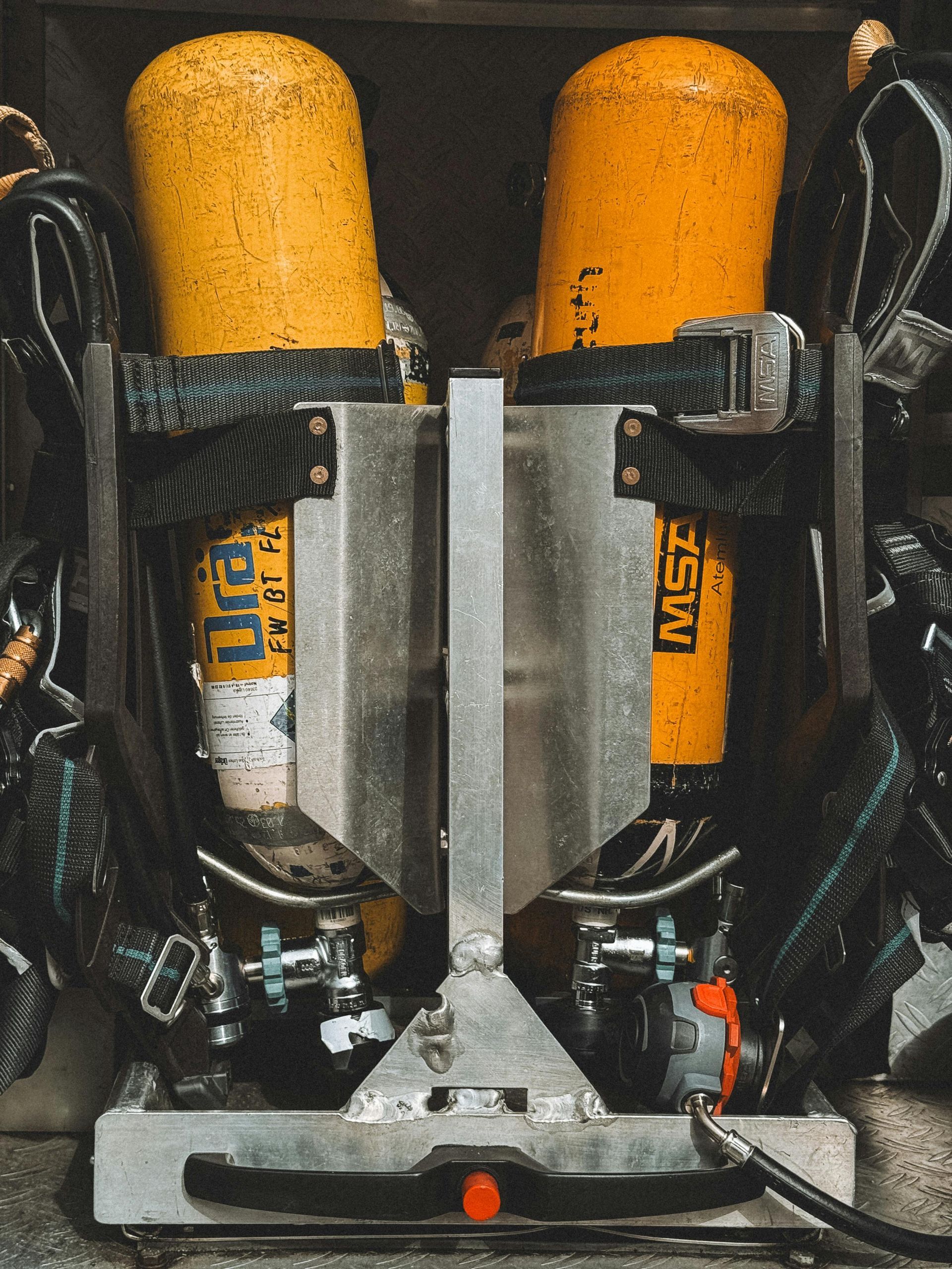Two orange air tanks secured in a black metal frame with a central silver divider and hose attachments