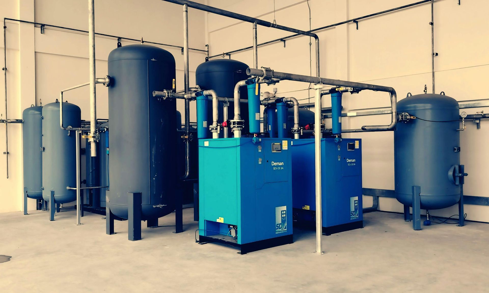 Blue industrial air compressor and tanks in a clean factory room with exposed piping.