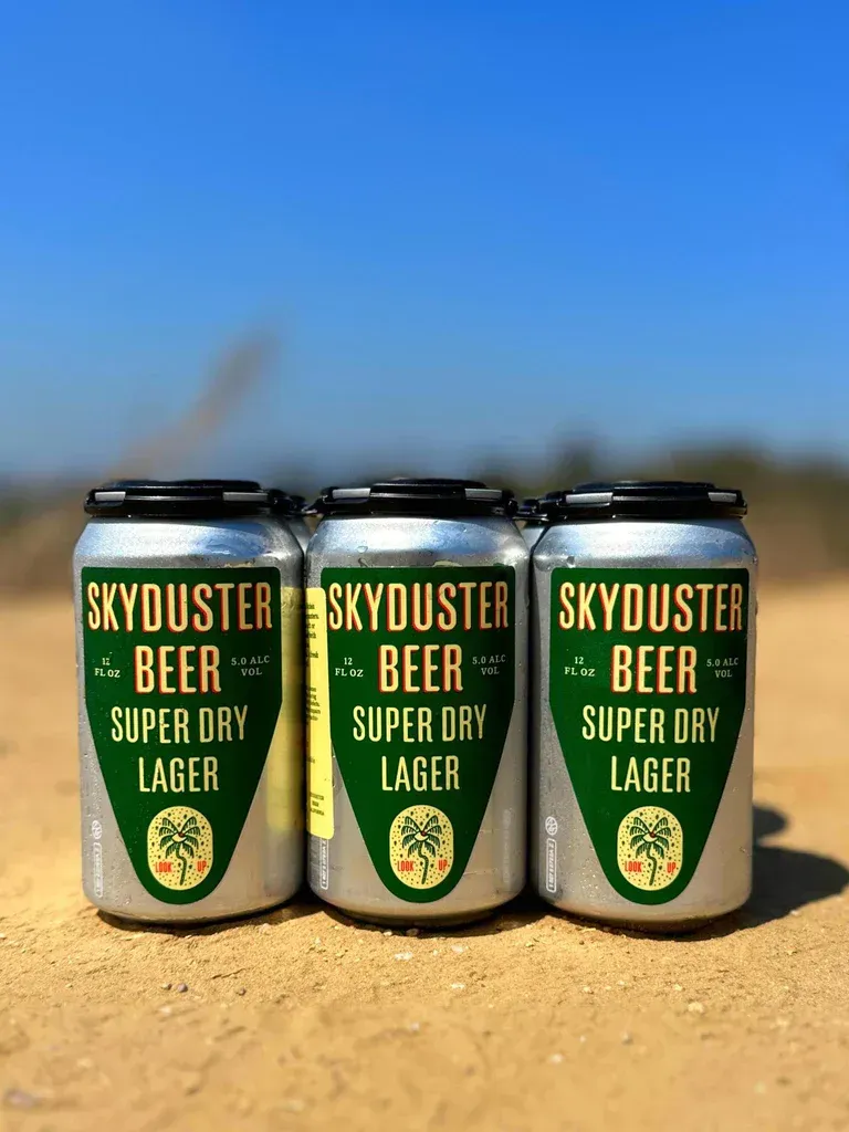 three cans of skyduster beer are sitting on top of a dirt field .