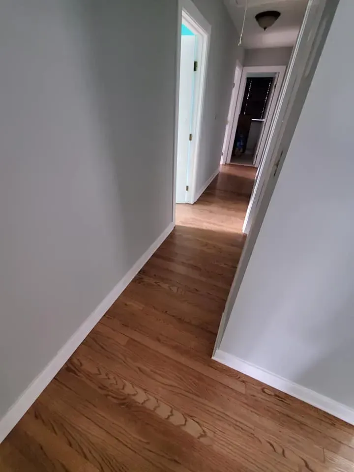 A hallway with hardwood floors and white trim in a house.