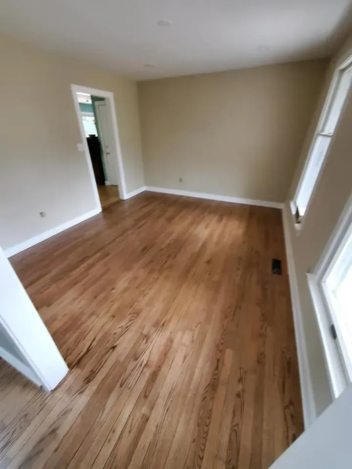An empty living room with hardwood floors and beige walls.