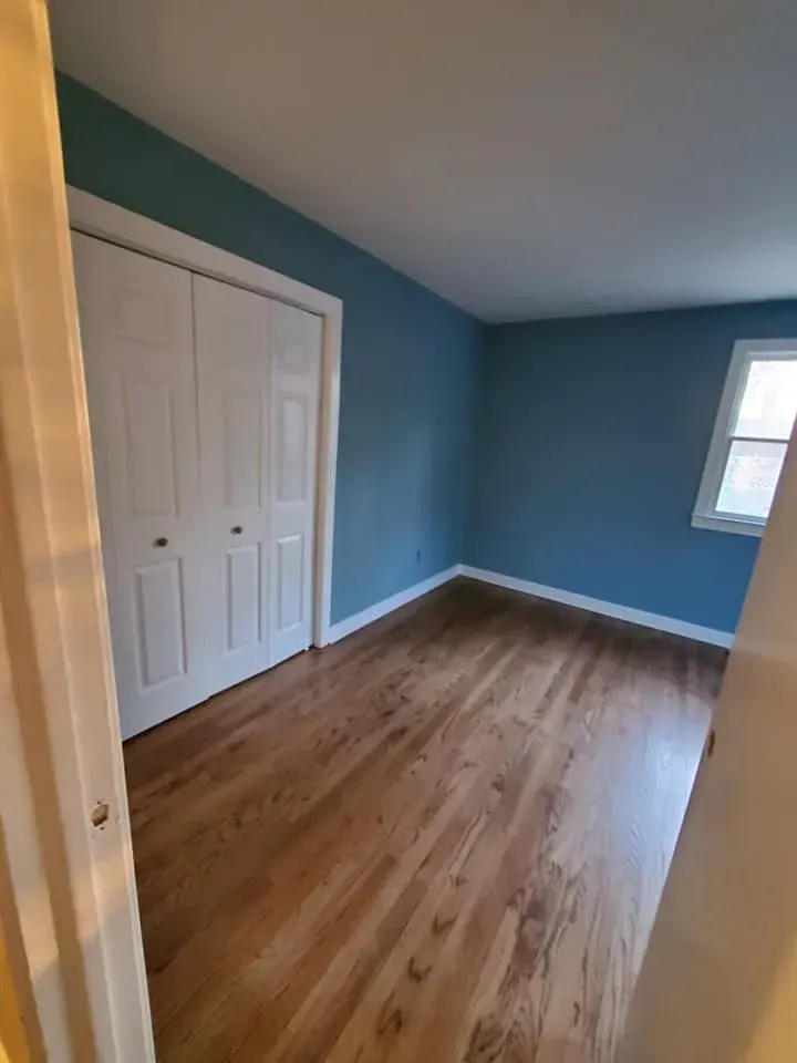 An empty bedroom with blue walls and hardwood floors.