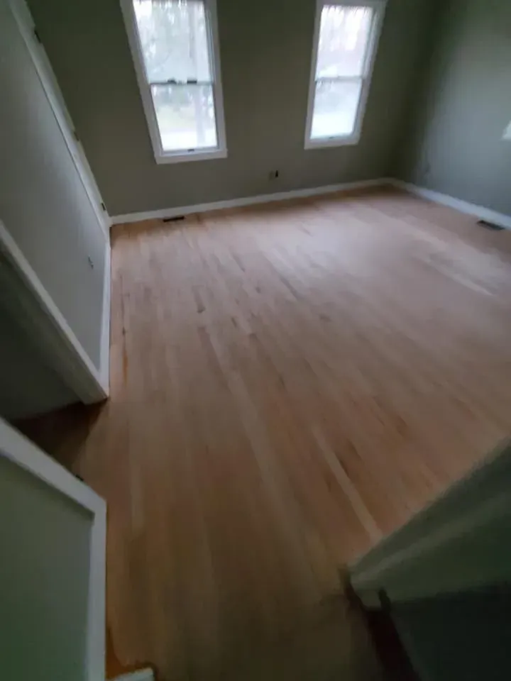 An empty room with hardwood floors and two windows.