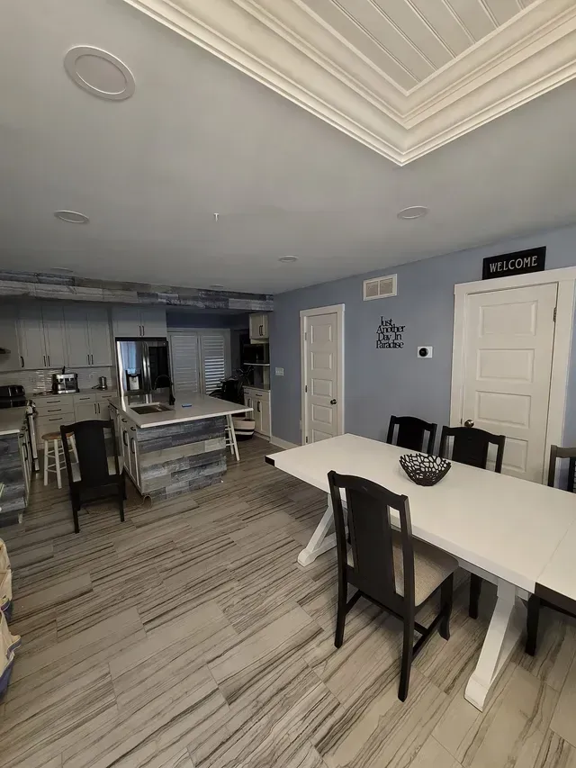A dining room with a table and chairs and a kitchen in the background.