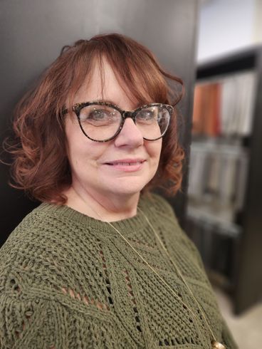 A woman wearing glasses and a green sweater is smiling for the camera.