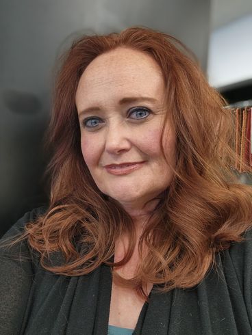 A woman with red hair and blue eyes is smiling for the camera.