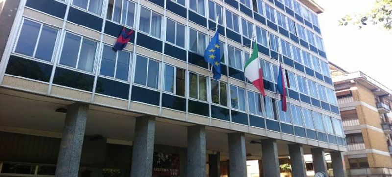 Facciata di un moderno edificio per uffici con vetrate, colonne e diverse bandiere all'ingresso.