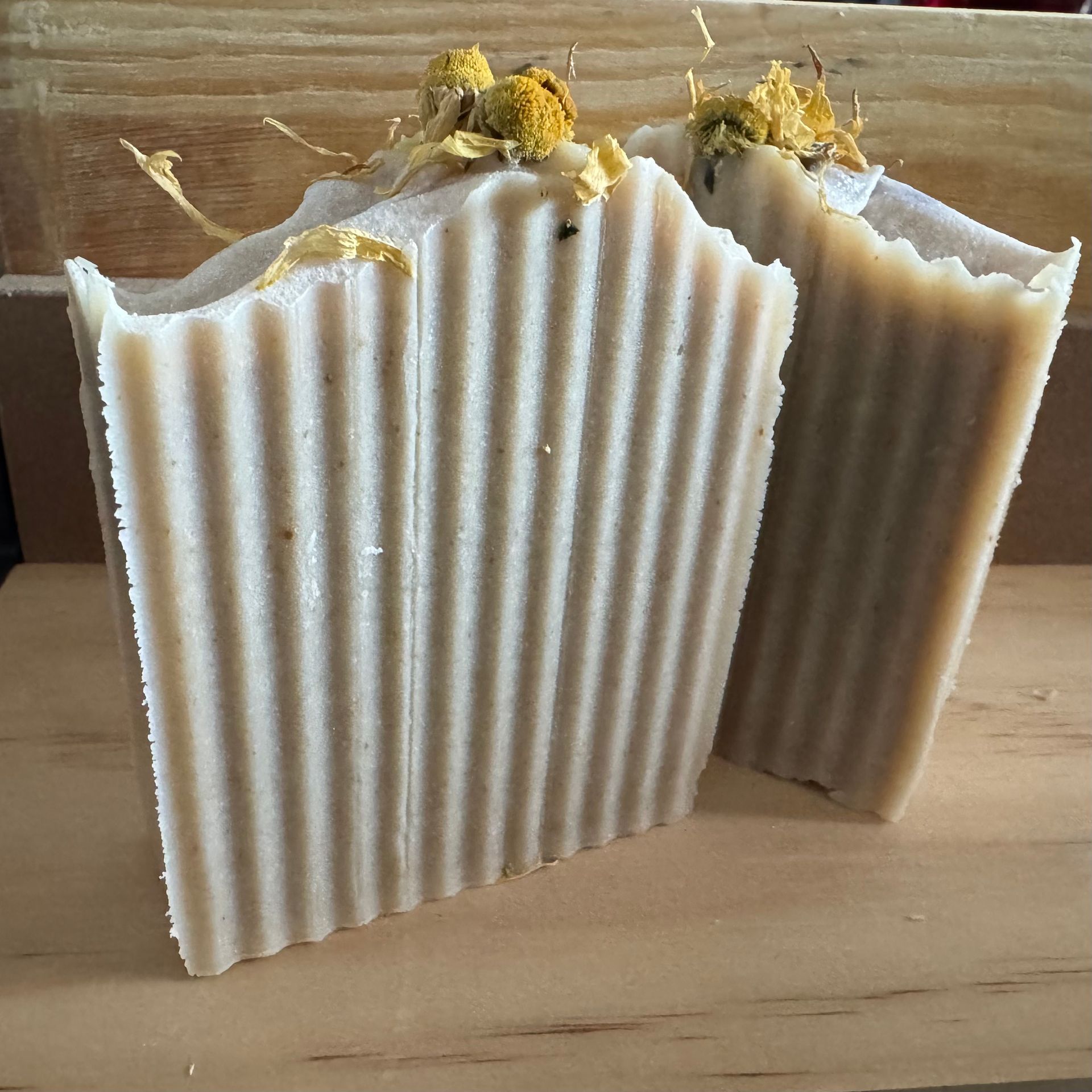 Two bars of textured, light brown soap, topped with dried flowers, on a wooden surface.