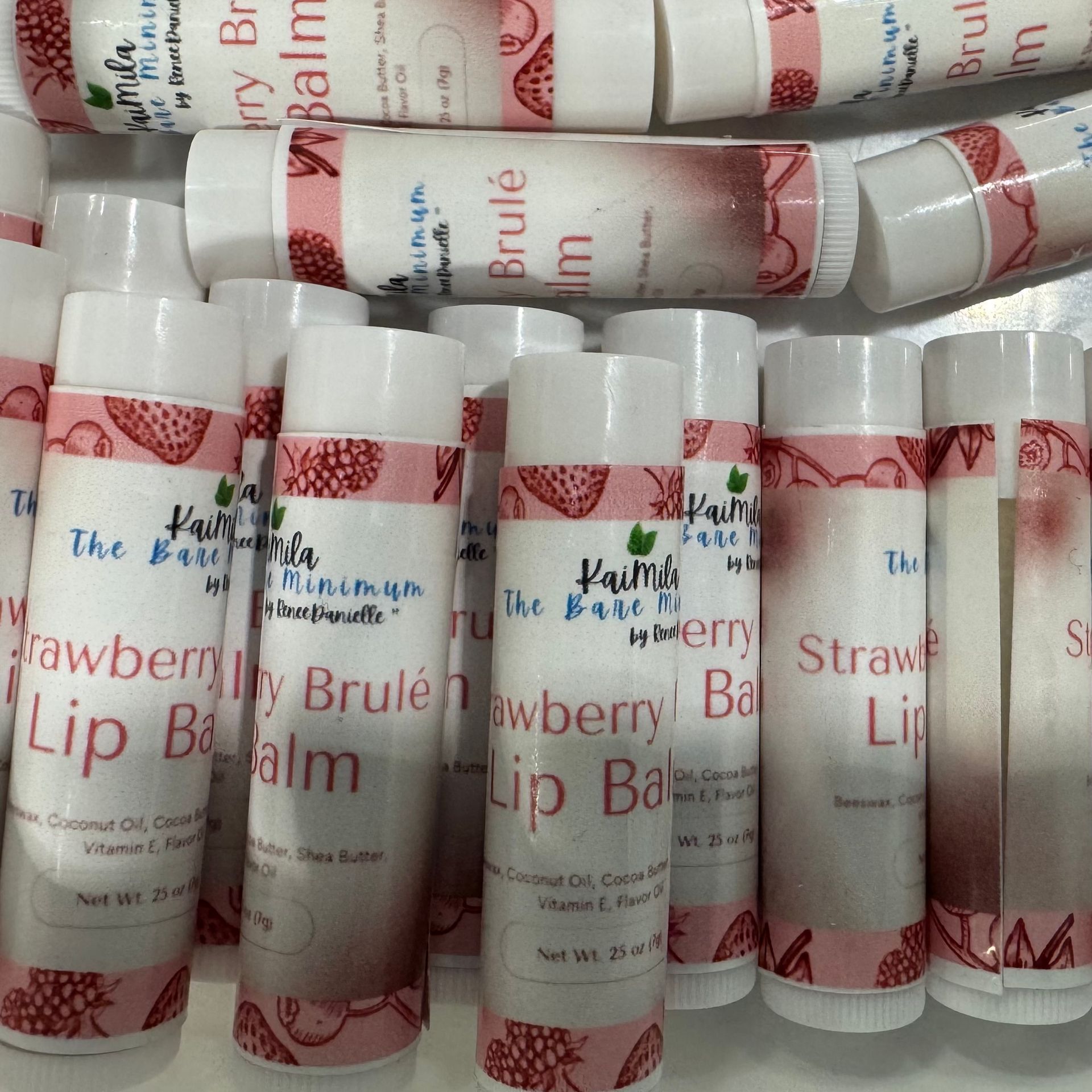 Pile of white lip balm tubes with pink strawberry labels.