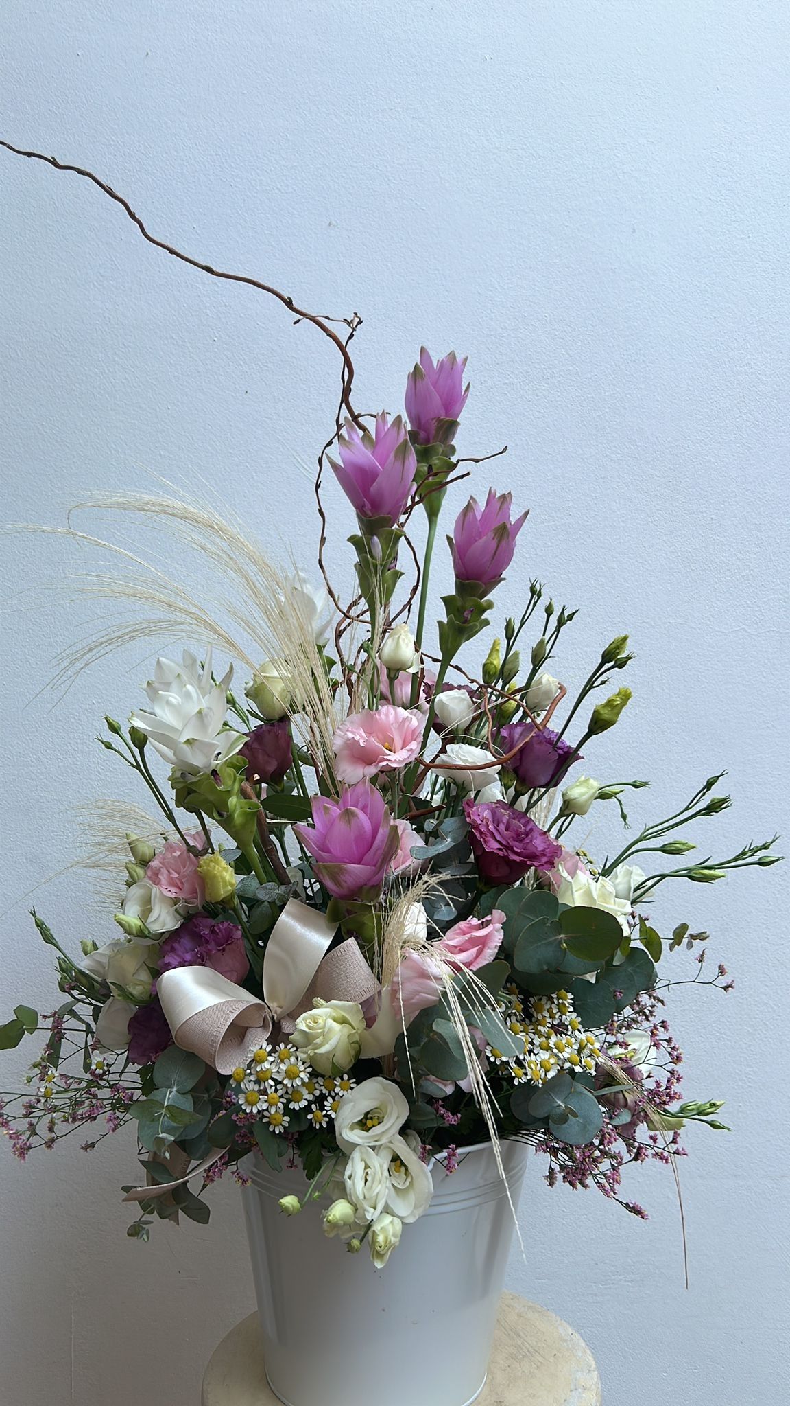 Composizione floreale in un vaso bianco, con fiori rosa, viola e bianchi, verde e un nastro.