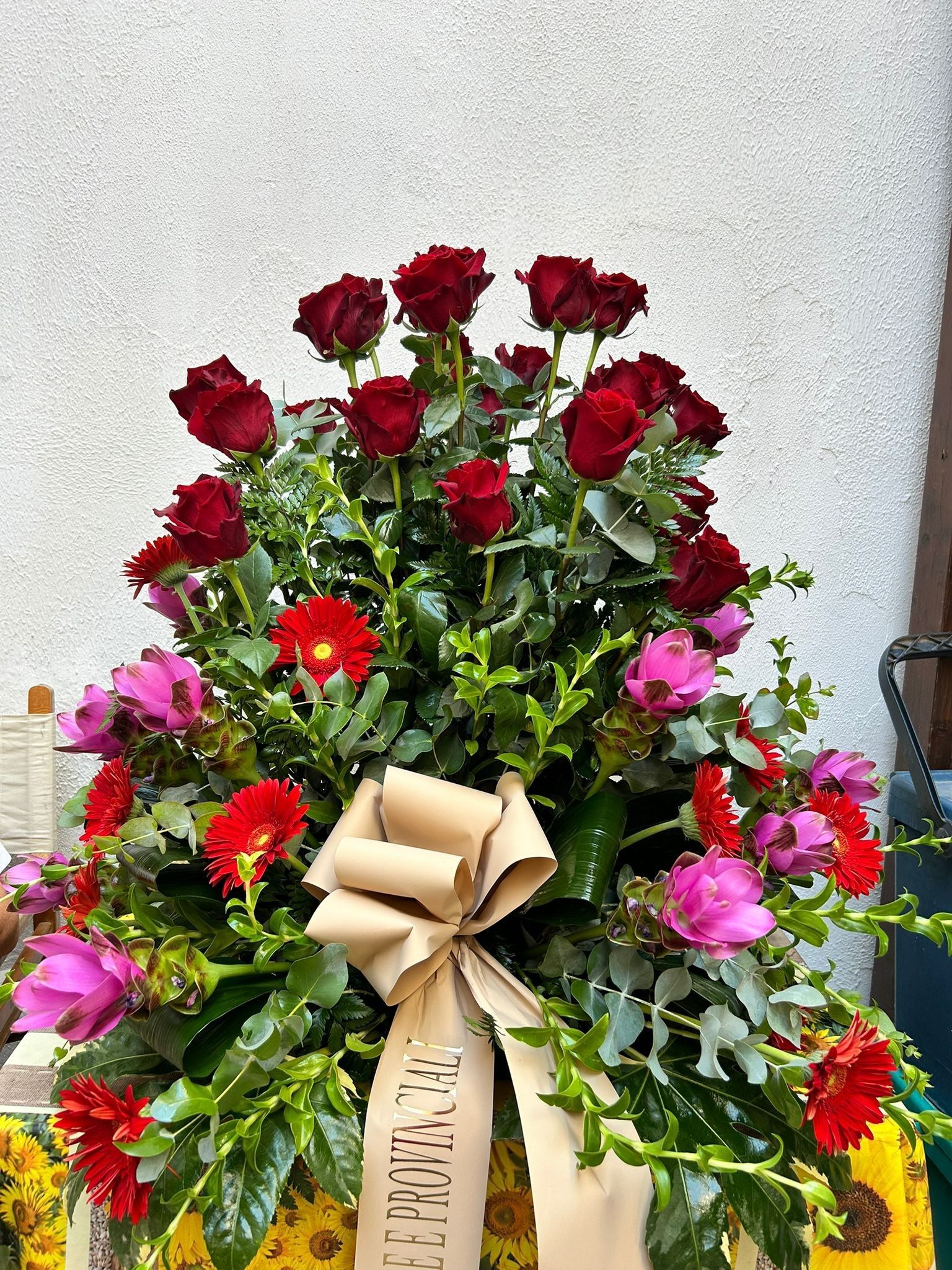 Composizione floreale di rose rosse, fiori rosa e rossi, con un nastro beige.