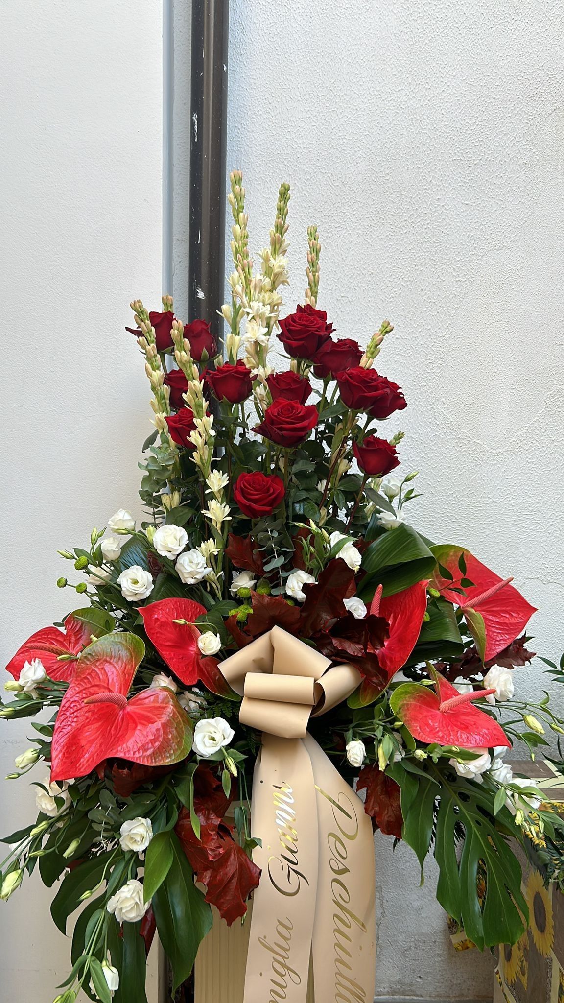 Composizione floreale con rose rosse, anthurium e un nastro.